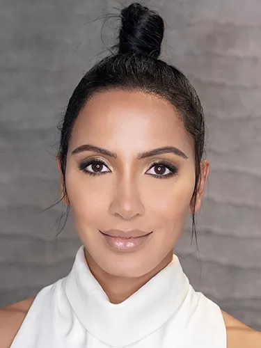 An image of a woman wearing white top and a ponytail looking happy and confident after her hairline lowering surgery